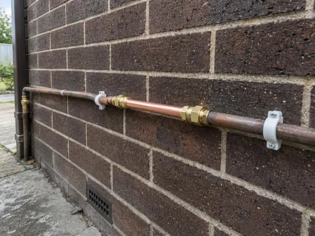 Repaired copper water pipe fixed to a dark brick exterior wall in Toronto