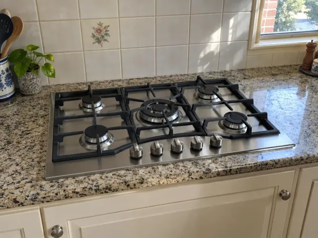 Stainless steel gas cooktop set into a speckled stone benchtop with tiled splashback in Awaba