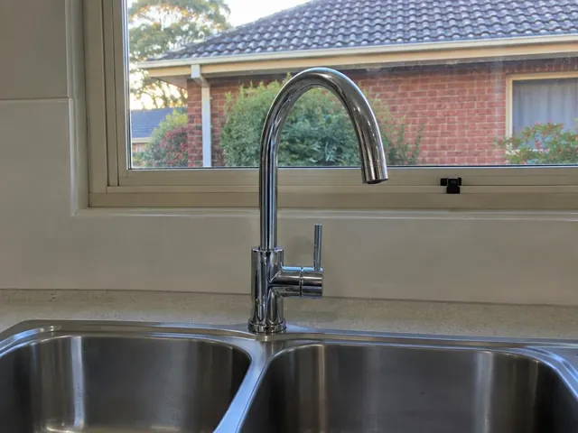 Chrome kitchen mixer tap above a double stainless steel sink beneath a window in Blackalls Park