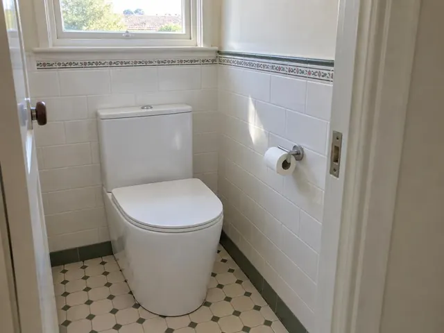 White toilet in a tiled bathroom with patterned floor and small window in Blackalls Park