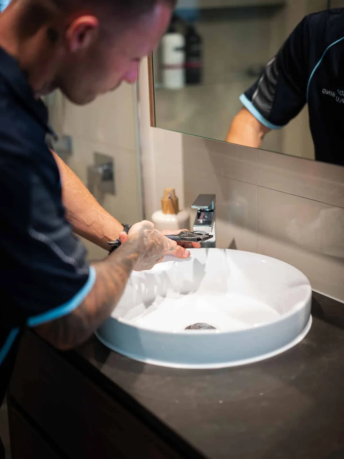 Plumber tightening a basin tap with a wrench