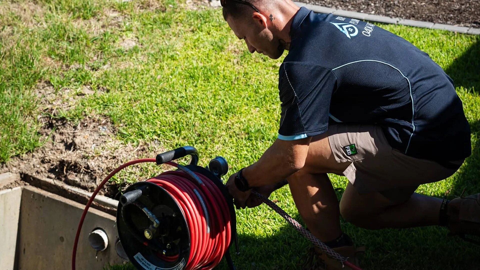 Plumber crouched at a drain pit feeding a high-pressure jetter hose
